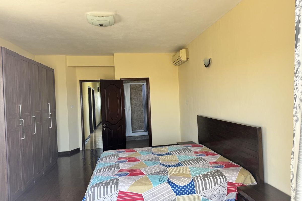 A spacious bedroom featuring dark wood laminate flooring, built-in wardrobes, and a wall-mounted air conditioning unit.