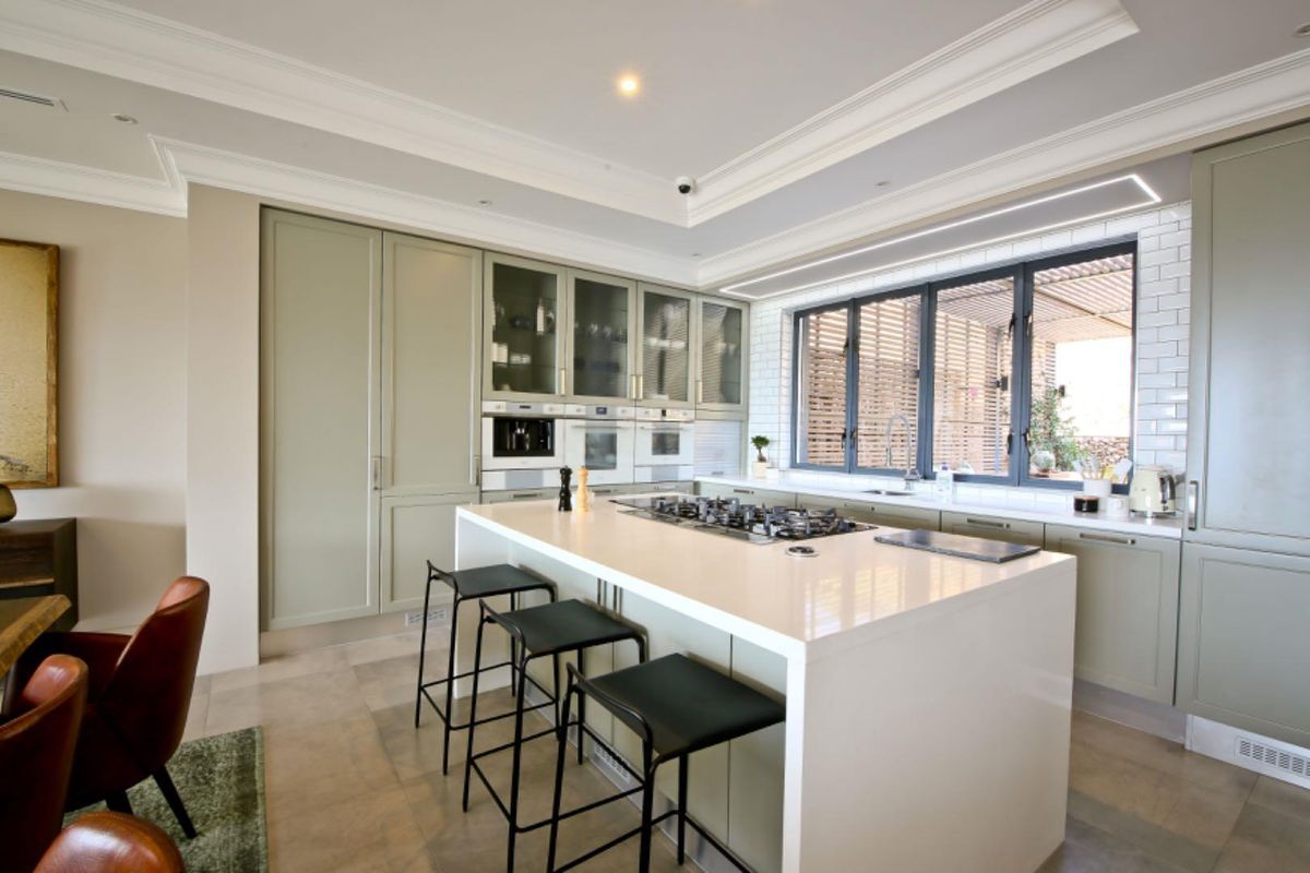 Modern kitchen featuring sage green cabinetry, a large central island with a built-in gas cooktop, stone countertops, and subway tile backsplash.