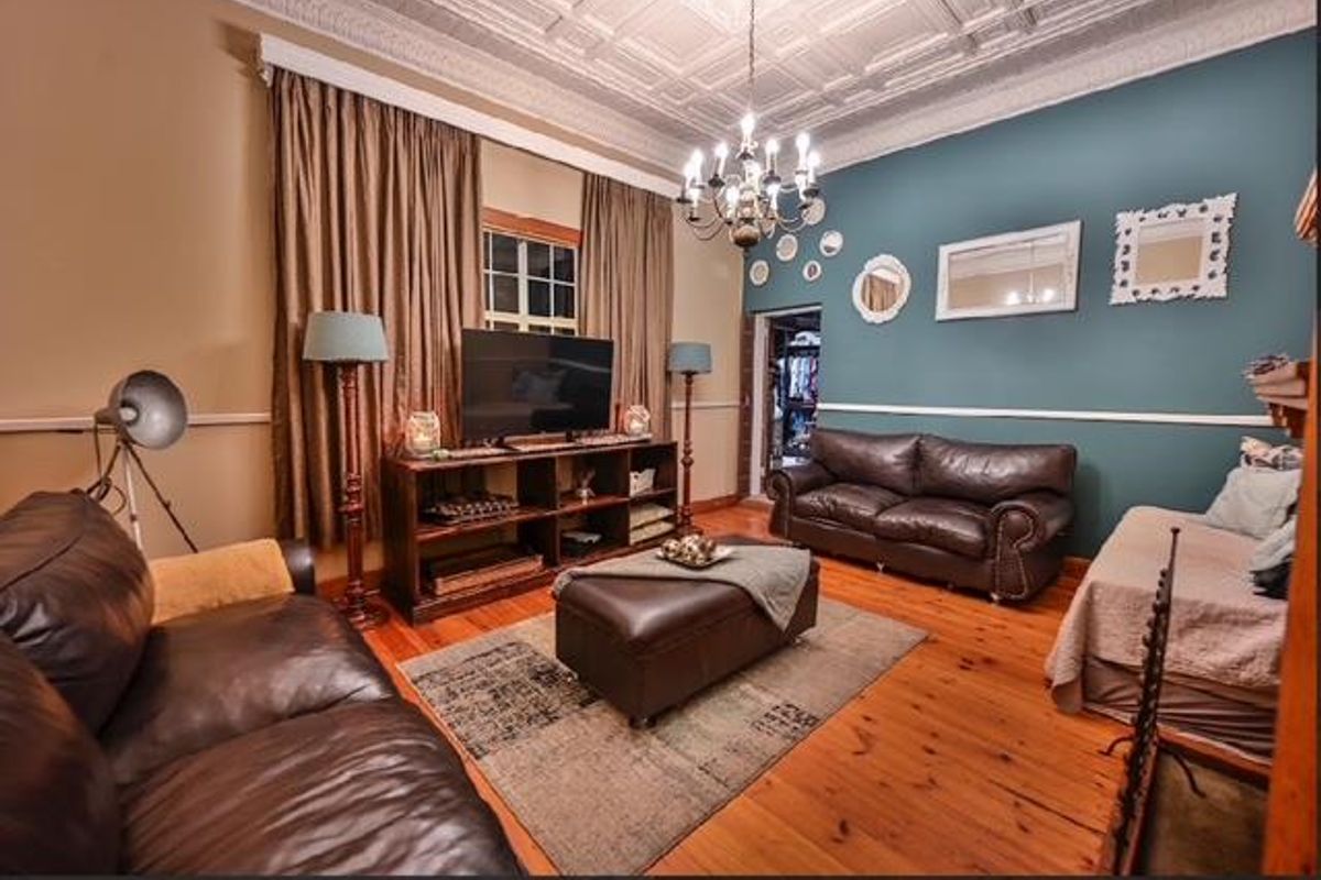 A character-filled living room featuring a decorative pressed metal ceiling, polished timber flooring, and a classic chair rail finish.