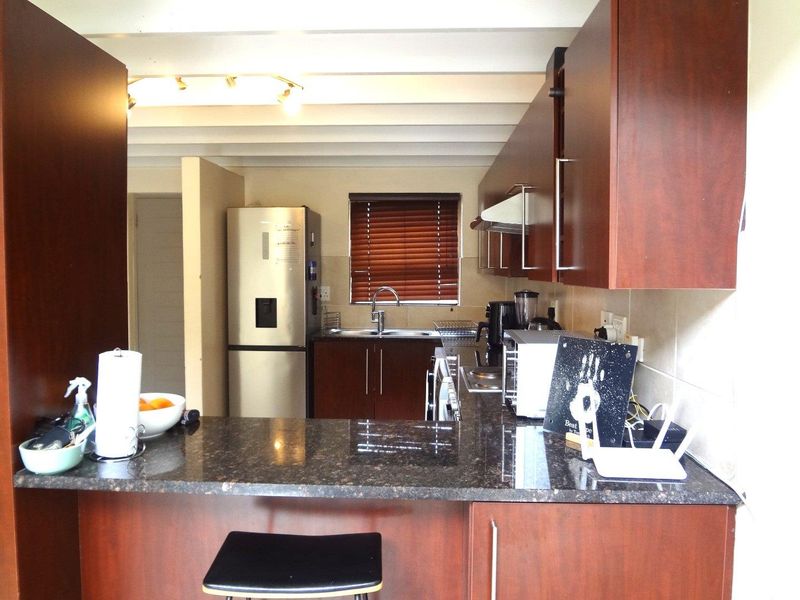 A functional kitchen featuring dark wood cabinetry, granite countertops, a breakfast bar, and a tiled backsplash with integrated extractor fan.