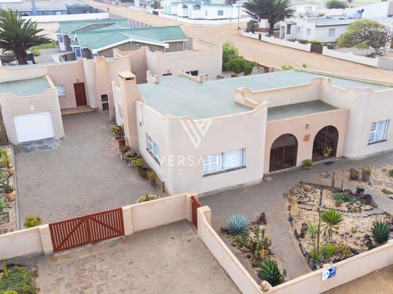 Aerial view of a residential property featuring a paved driveway, garage, gated entrance, and established garden areas.