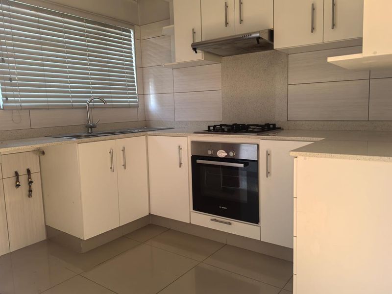 A clean, modern kitchen featuring white cabinetry, stone countertops, a gas hob, built-in oven, and stainless steel sink with tiled splashback.