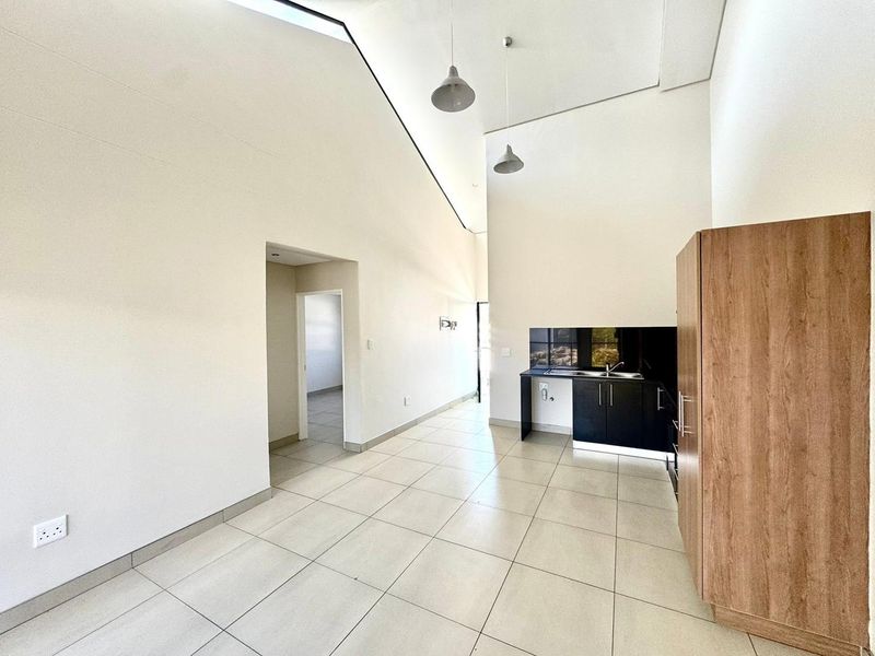 An open-plan living area featuring high vaulted ceilings, tiled flooring, and a compact kitchenette with modern cabinetry and a stainless steel sink.