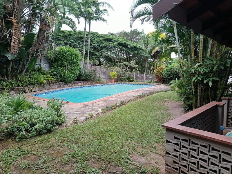 A private outdoor pool area featuring stone paving, brick coping, and established garden landscaping with mature trees.