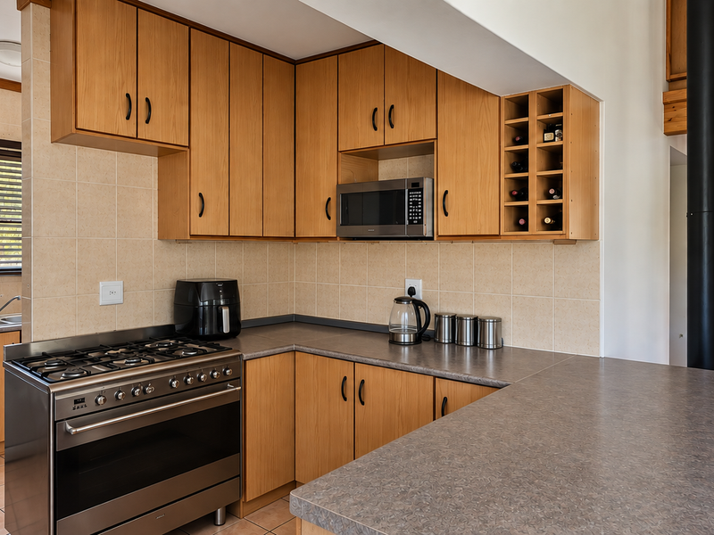 A functional kitchen featuring light wood cabinetry, gas stove, built-in microwave, and a breakfast bar, adjacent to a wooden staircase leading to a loft area.