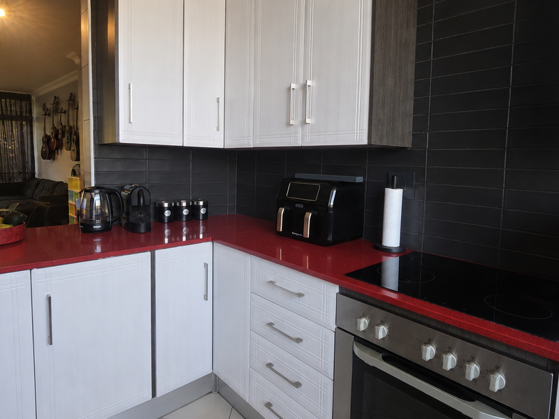 A modern kitchen featuring white cabinetry, striking red countertops, and a black subway tile backsplash, equipped with a built-in oven and electric cooktop.