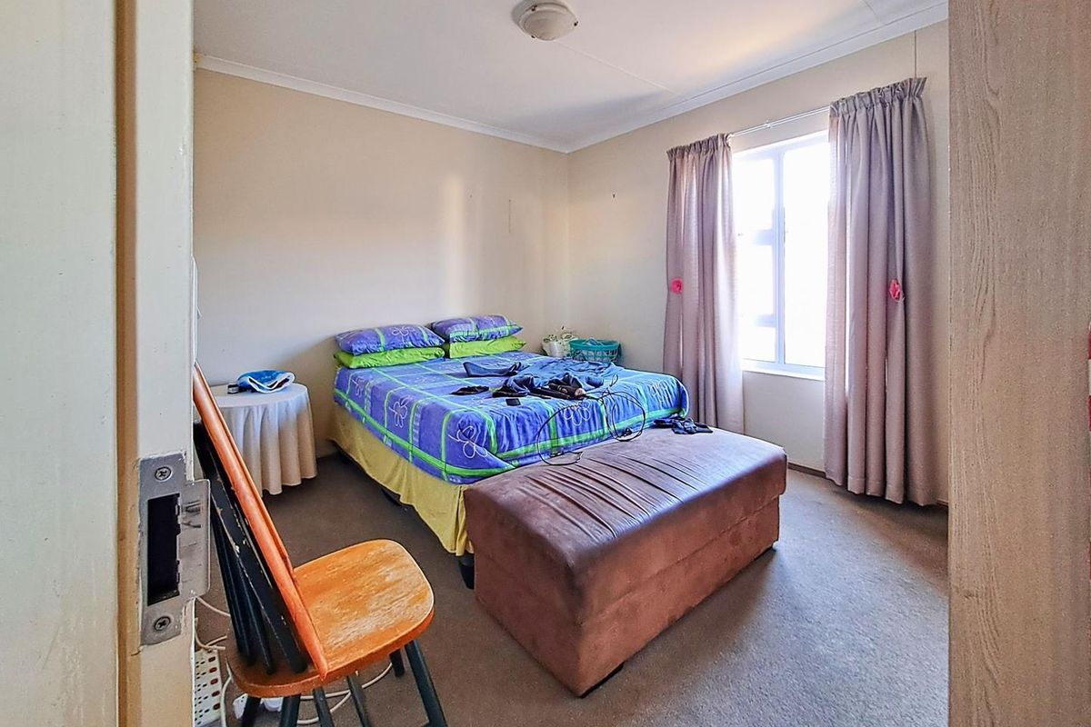 A standard bedroom featuring neutral wall tones, carpeted flooring, and a window with curtain tracks, providing a functional living space.