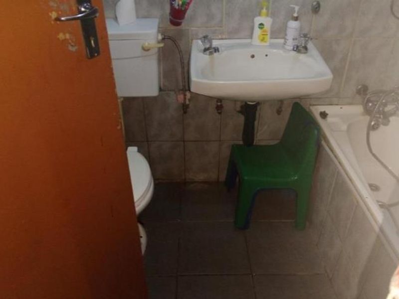 Compact bathroom featuring a pedestal washbasin, toilet, and bathtub with tiled walls and flooring, requiring cosmetic updates to modernize the space.
