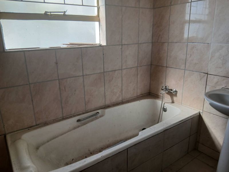 A dated bathroom featuring a bathtub, pedestal basin, and tiled walls, currently in need of renovation and deep cleaning to restore its functionality.