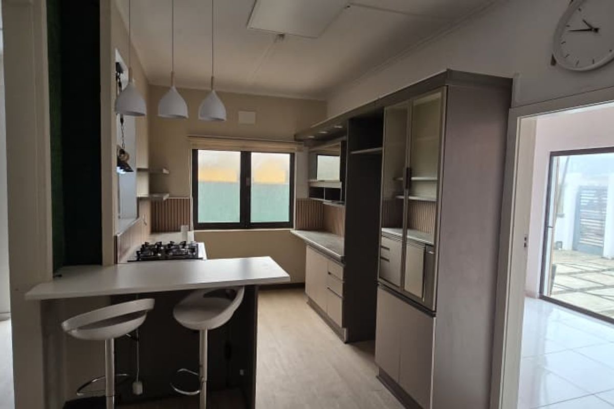 Modern kitchen featuring a breakfast bar, built-in cabinetry, and a gas cooktop, seamlessly flowing into the adjacent living and outdoor areas.