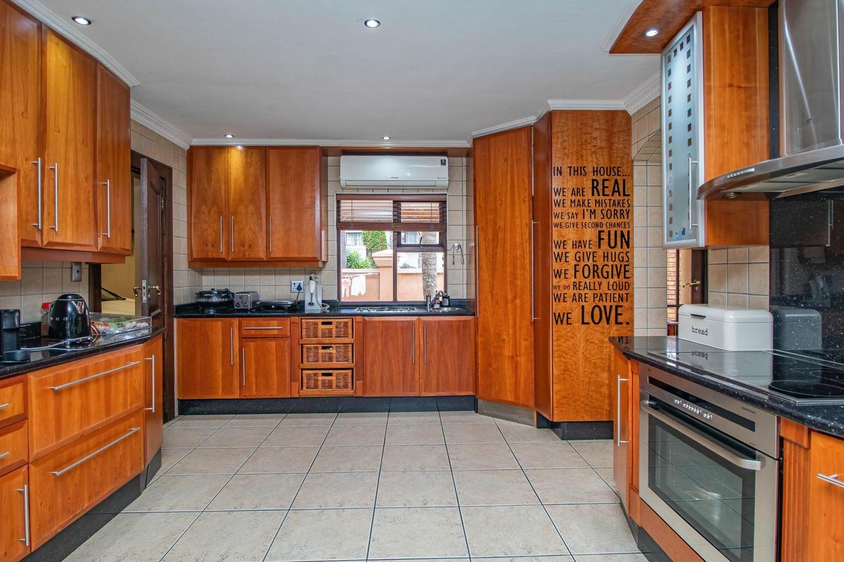 A functional kitchen featuring warm-toned wooden cabinetry, dark granite countertops, tiled flooring, and integrated appliances including an oven and extractor fan.