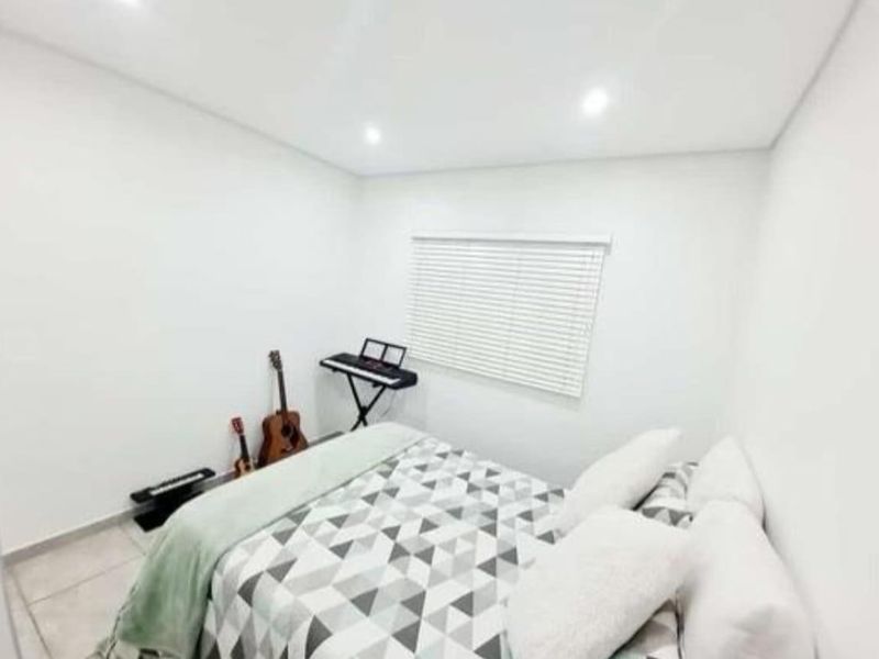 A bright and neutral bedroom featuring tiled flooring, recessed downlighting, and venetian blinds, offering a clean and modern living space.