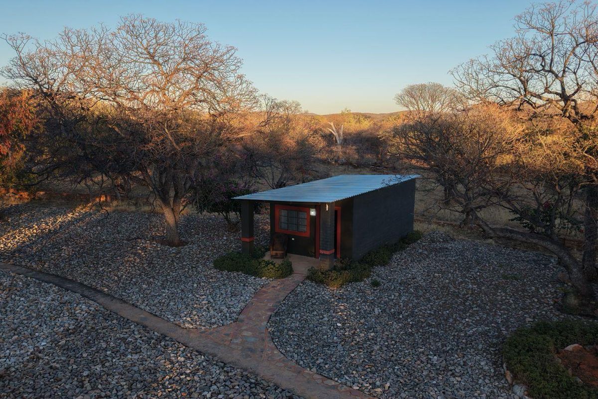 An aerial view of a detached lodge unit featuring a corrugated metal roof, covered porch, and stone pathway set within a natural landscape.