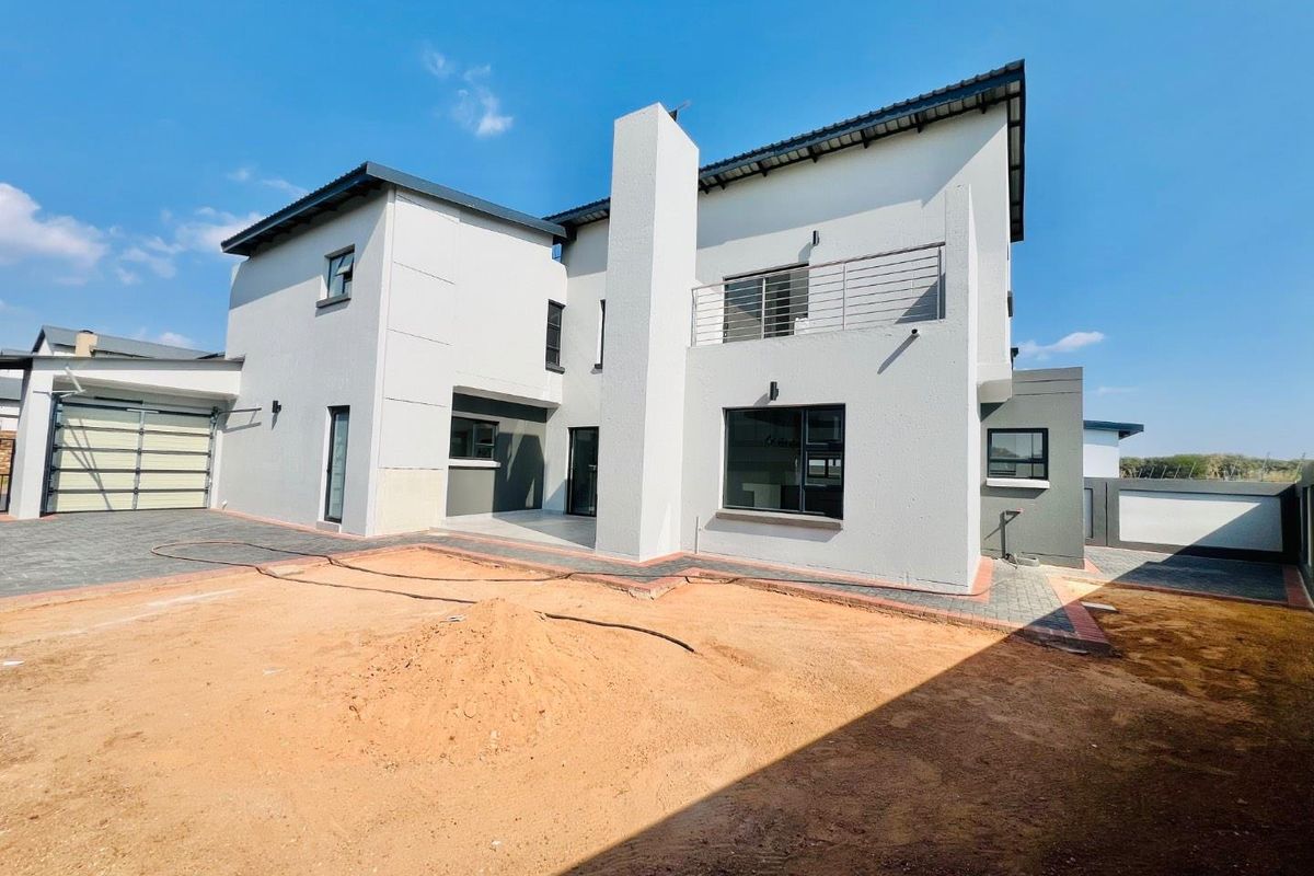 Rear view of a modern double-storey cluster home featuring a balcony, paved driveway, and an unlandscaped garden area ready for final finishing.