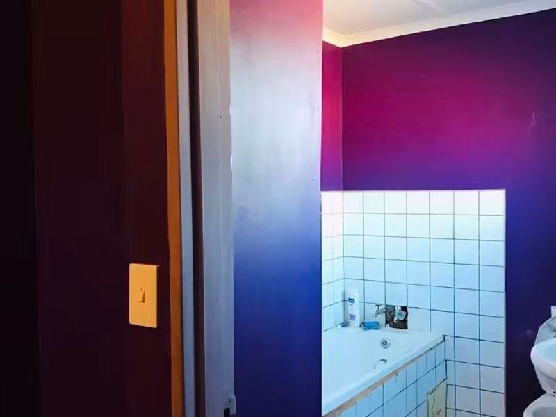 A bathroom featuring a bathtub and toilet with tiled finishes, currently finished in a bold purple paint scheme.