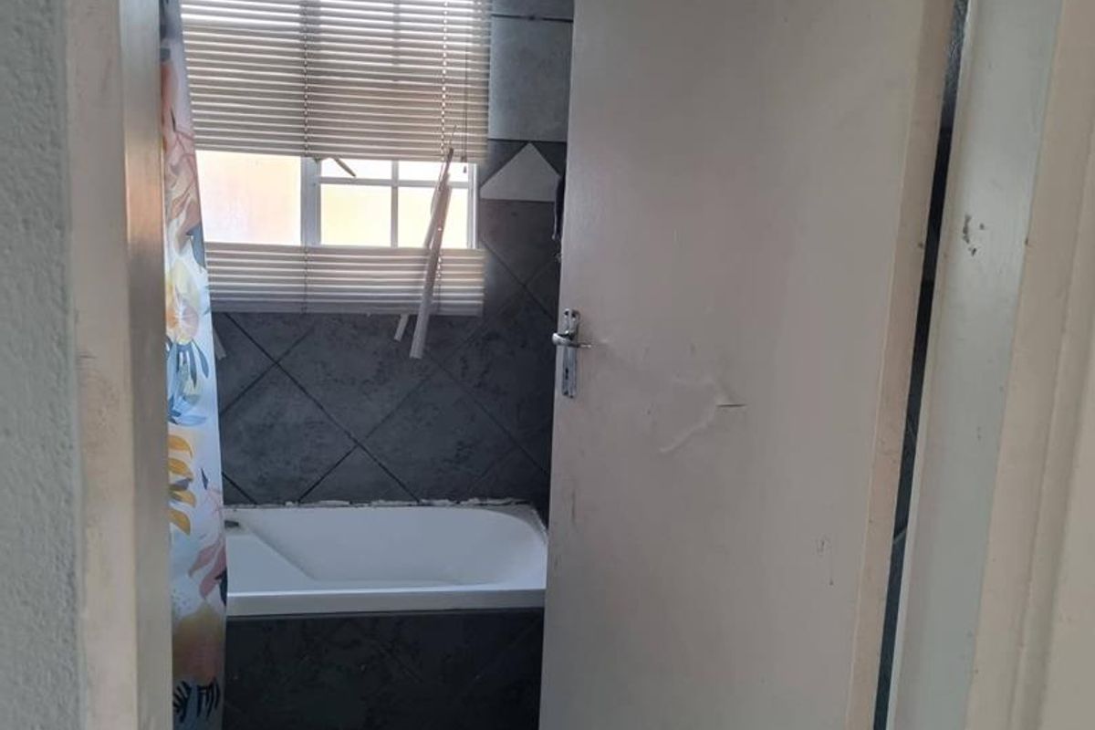 A compact bathroom featuring a built-in bathtub with tiled surround and a window with fitted blinds.