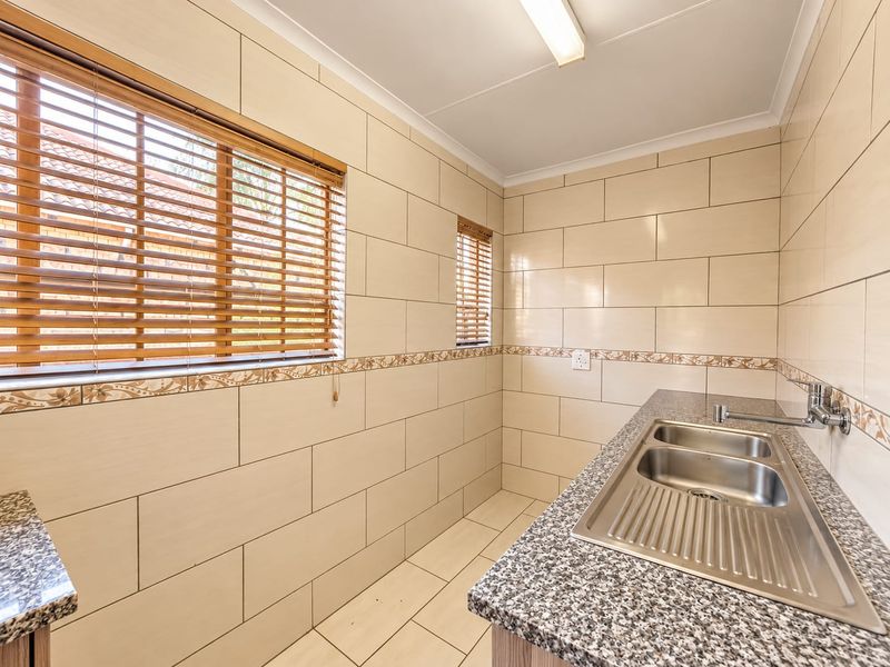 A clean and functional scullery featuring tiled walls, granite countertops, and a double stainless steel sink with ample space for appliances.