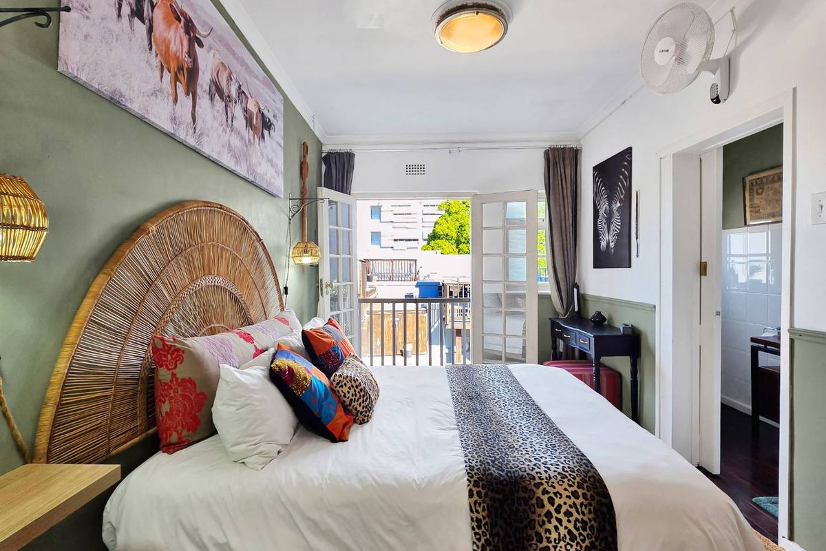 A well-lit bedroom featuring timber flooring, a ceiling fan, and direct access to a private balcony through classic french doors.