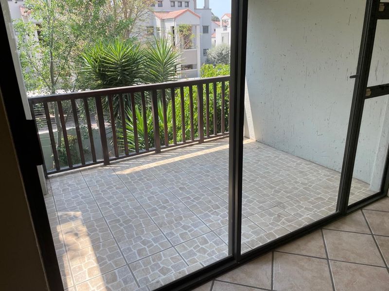 A private balcony featuring tiled flooring and a safety railing, accessible through a sliding glass door, offering an outdoor space for relaxation.