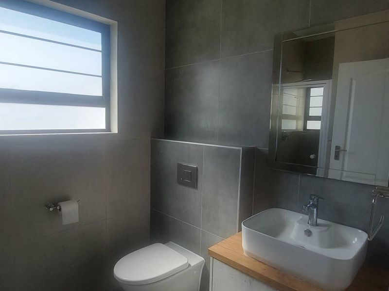 Modern bathroom featuring a wall-mounted toilet with concealed cistern, vessel sink on a wooden vanity, and contemporary grey wall tiling.