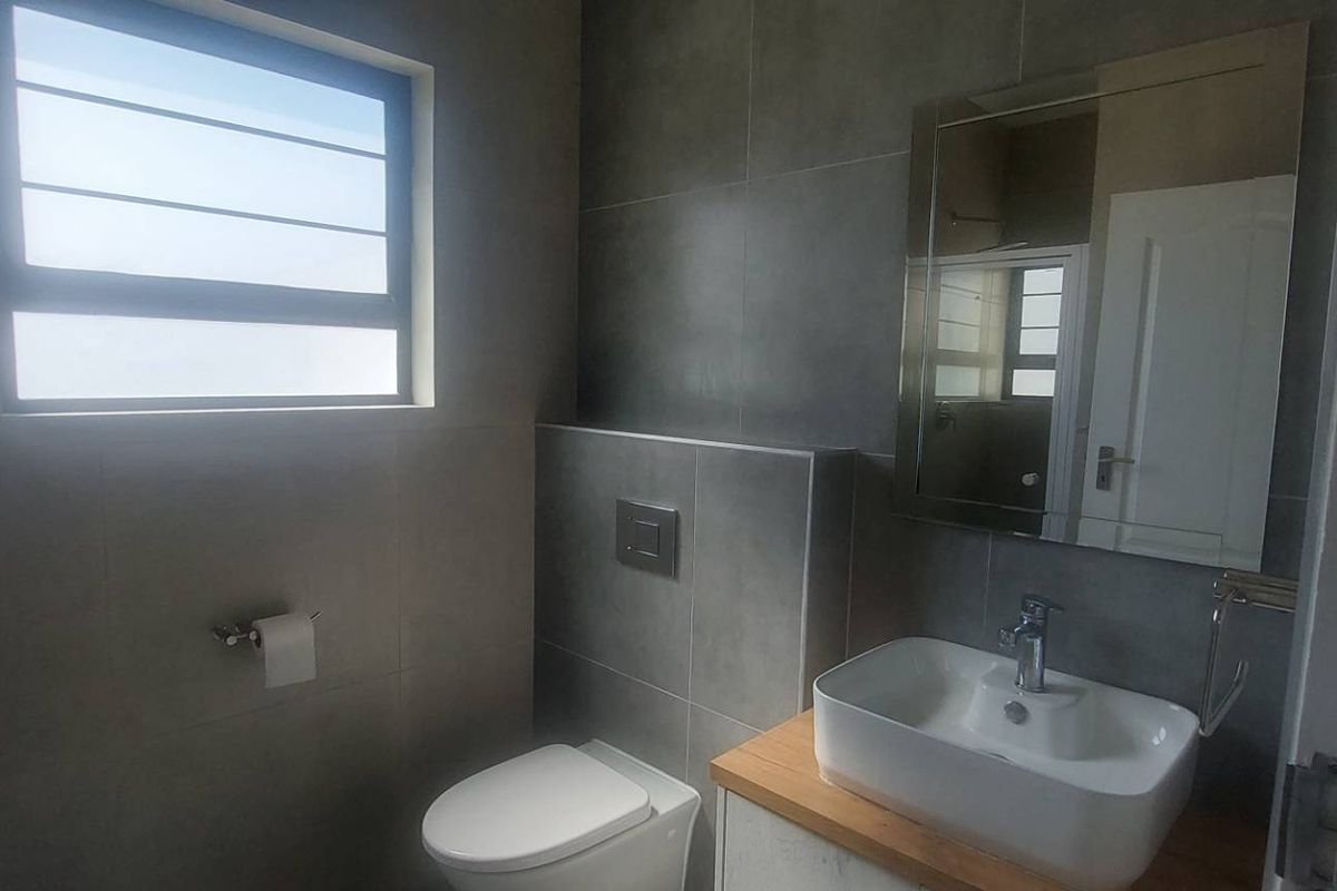 Modern bathroom featuring a wall-mounted toilet with concealed cistern, vessel sink on a wooden vanity, and contemporary grey wall tiling.