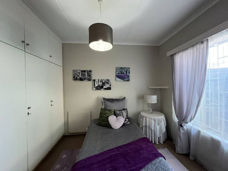 A well-maintained bedroom featuring built-in cupboards, neutral wall finishes, and a window fitted with security bars for added peace of mind.