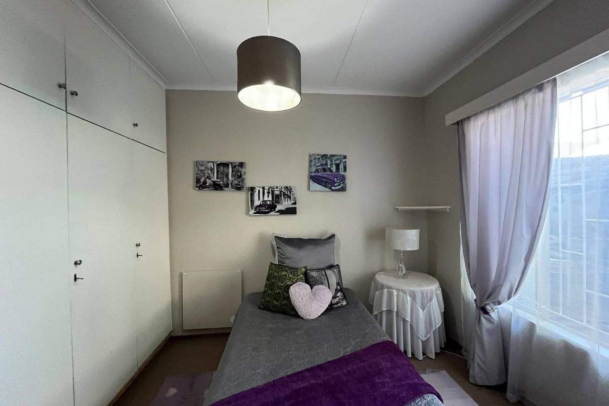 A well-maintained bedroom featuring built-in cupboards, neutral wall finishes, and a window fitted with security bars for added peace of mind.