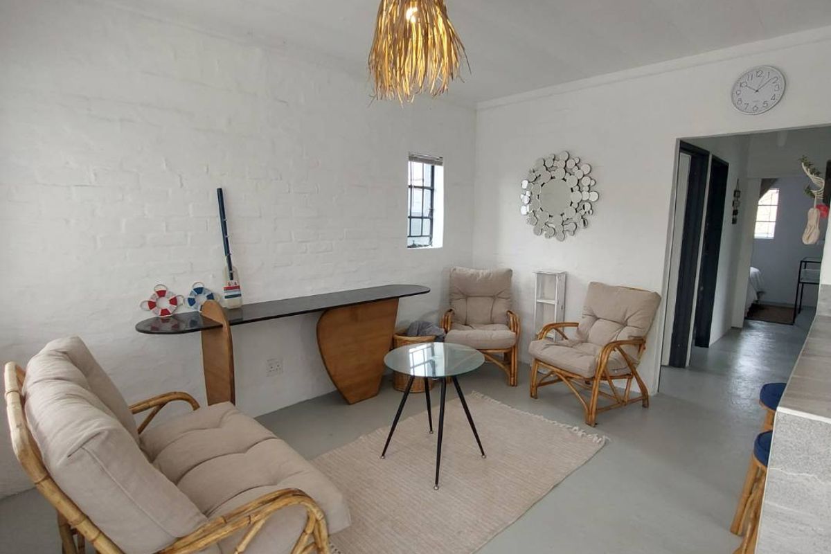 A bright living area featuring painted brick walls, a neutral concrete floor, and a central pendant light fixture, offering a clean and simple aesthetic.
