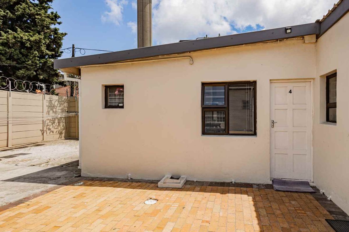 Exterior view of the apartment unit featuring a paved courtyard area, secure door access, and window with blinds.
