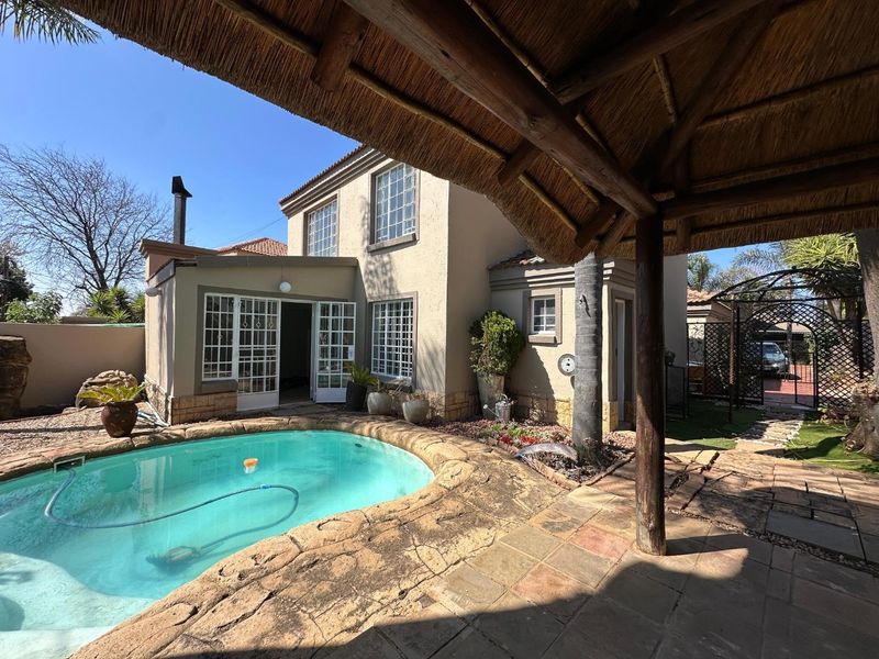Rear exterior view featuring a swimming pool, stone paved patio area, and a traditional thatched lapa structure.