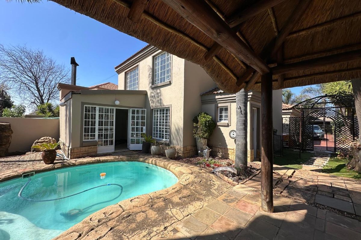 Rear exterior view featuring a swimming pool, stone paved patio area, and a traditional thatched lapa structure.