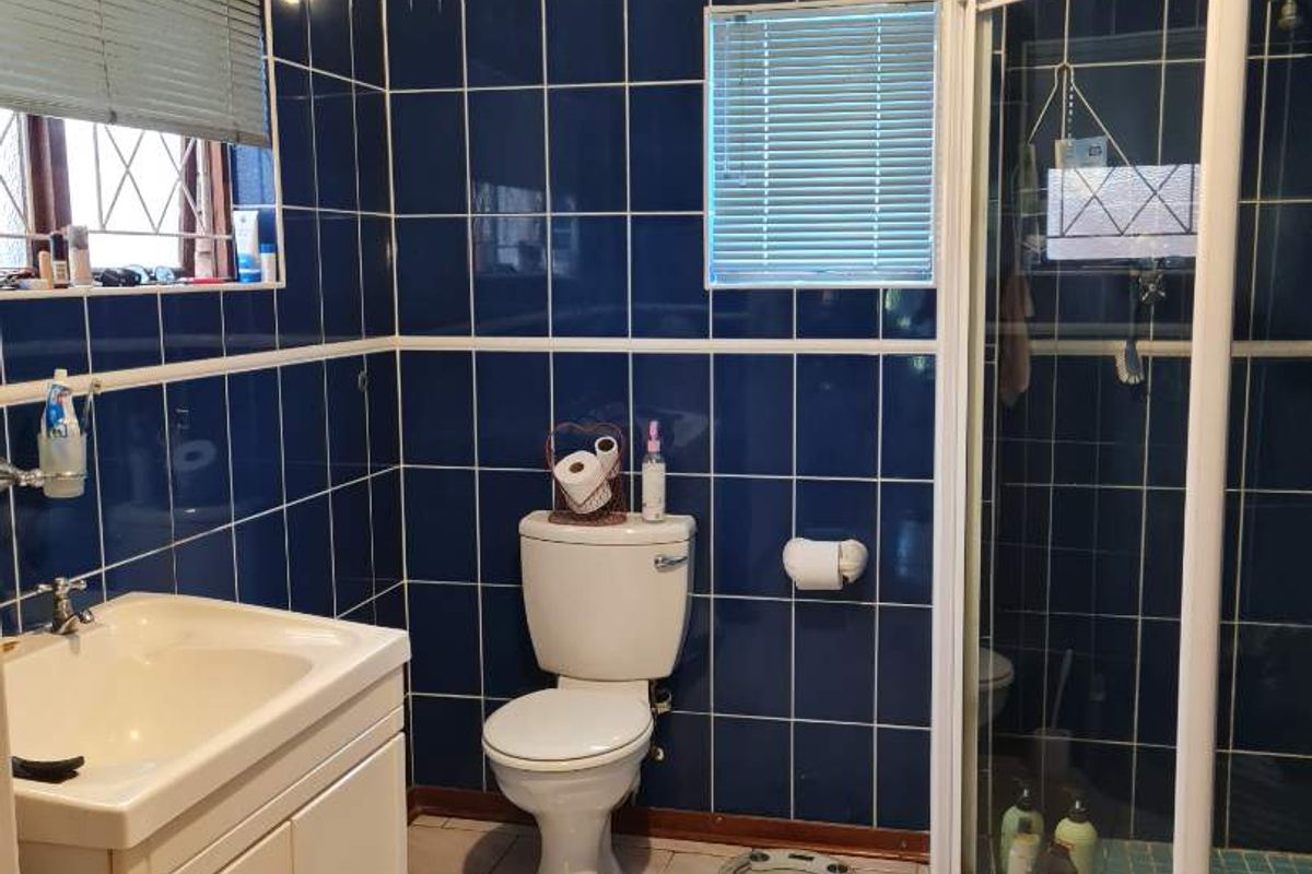 A functional bathroom featuring a corner shower enclosure, a vanity basin, and a toilet, finished with dark blue wall tiles and light floor tiles.