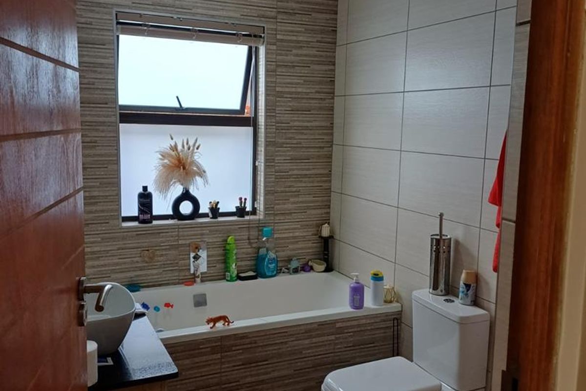 A modern bathroom featuring a built-in bathtub with tiled surround, a wall-mounted toilet, and a vanity basin with a dark countertop.