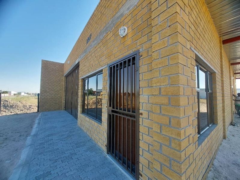 Exterior view of an industrial building featuring exposed brickwork, secure metal gate, aluminium window frames, and a paved walkway.