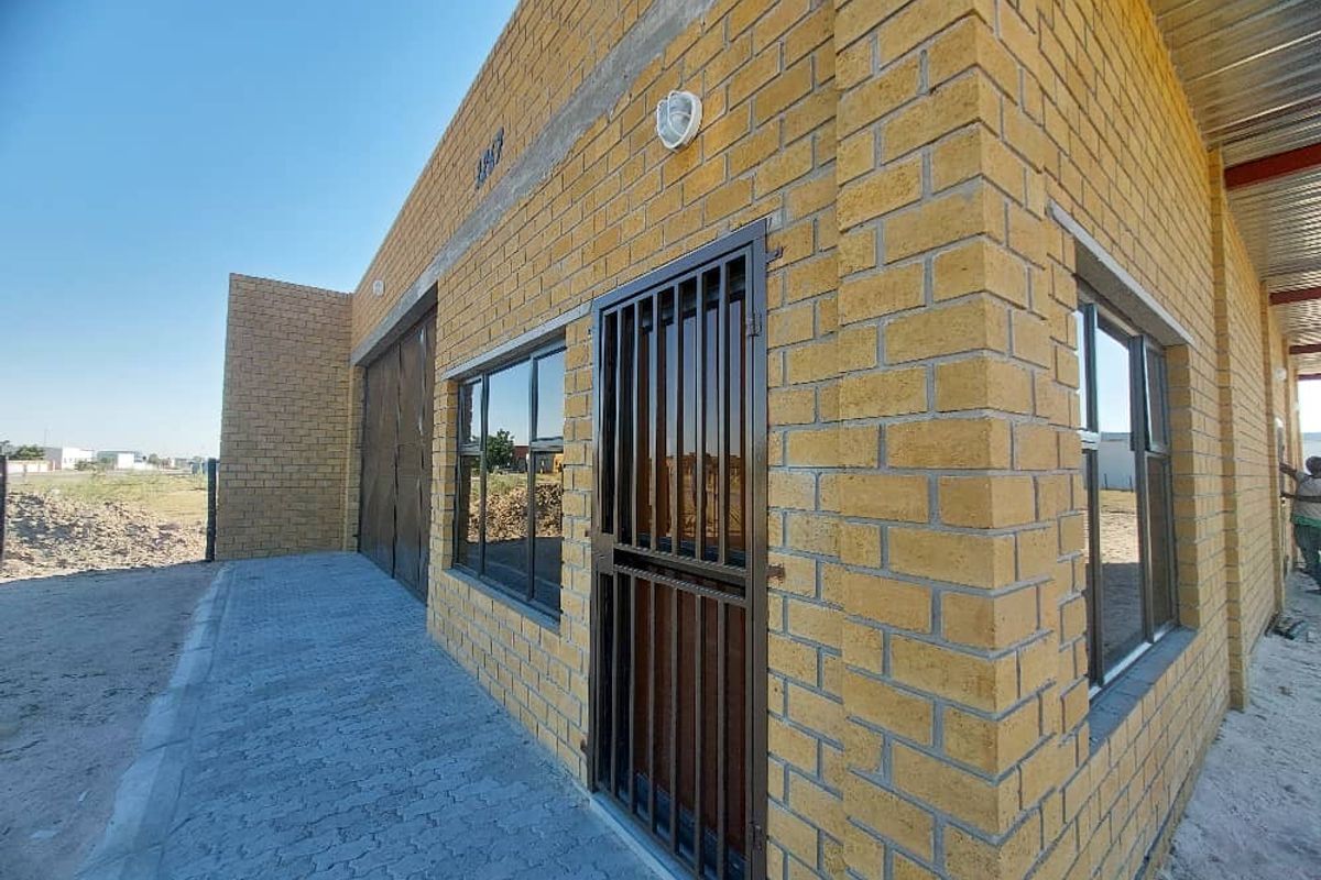 Exterior view of an industrial building featuring exposed brickwork, secure metal gate, aluminium window frames, and a paved walkway.
