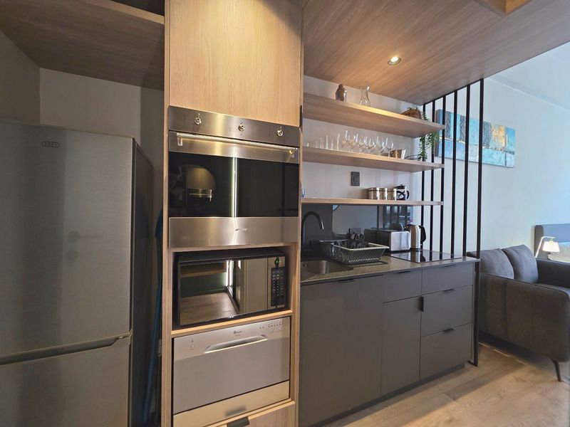 Modern compact kitchen featuring sleek cabinetry, built-in appliances including an oven and microwave, integrated dishwasher, and stylish open shelving with a decorative metal divider.