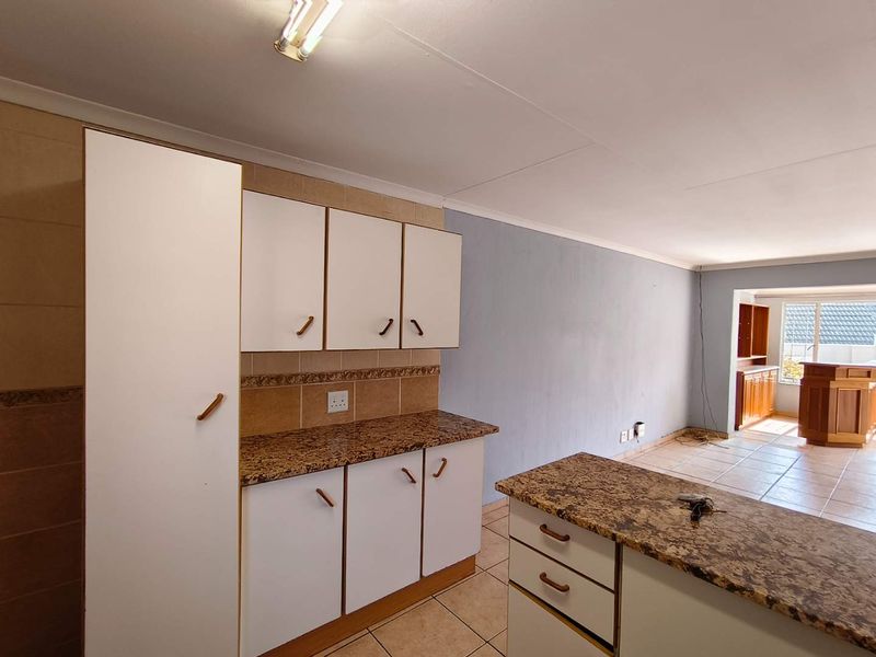 Open plan kitchen area featuring granite countertops, tiled flooring, and built-in cabinetry, flowing into an adjacent living space.