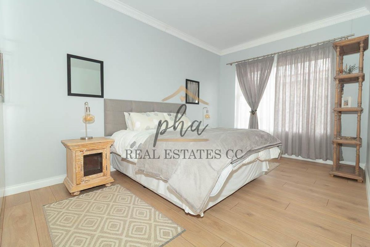 A well-maintained bedroom featuring light-toned laminate flooring, neutral wall paint, and crown molding, providing a clean and comfortable living space.
