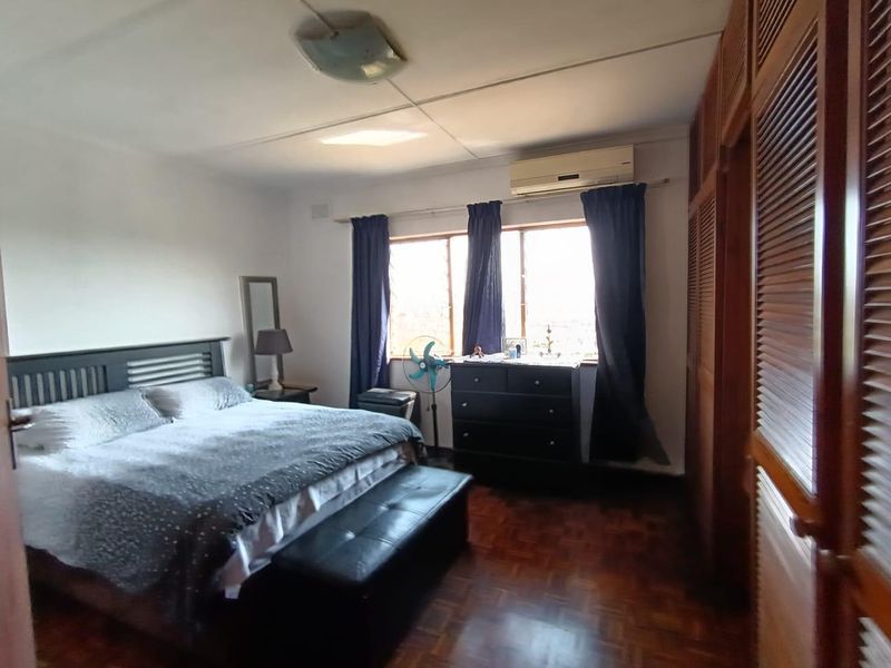 A spacious bedroom featuring warm parquet flooring, extensive built-in wooden cabinetry, and a wall-mounted air conditioning unit for climate control.