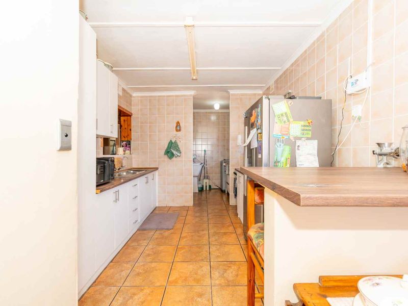 A functional kitchen featuring tiled walls and flooring, built-in cabinetry, and a laminate countertop, offering a dated aesthetic ready for modernization.
