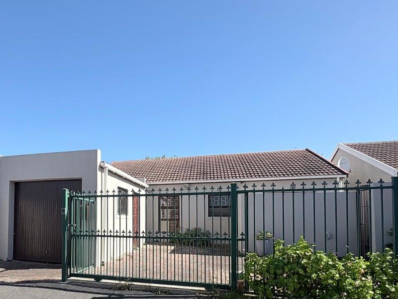 Front view of the property featuring a paved driveway, secure metal gate, and attached garage with a tiled roof.