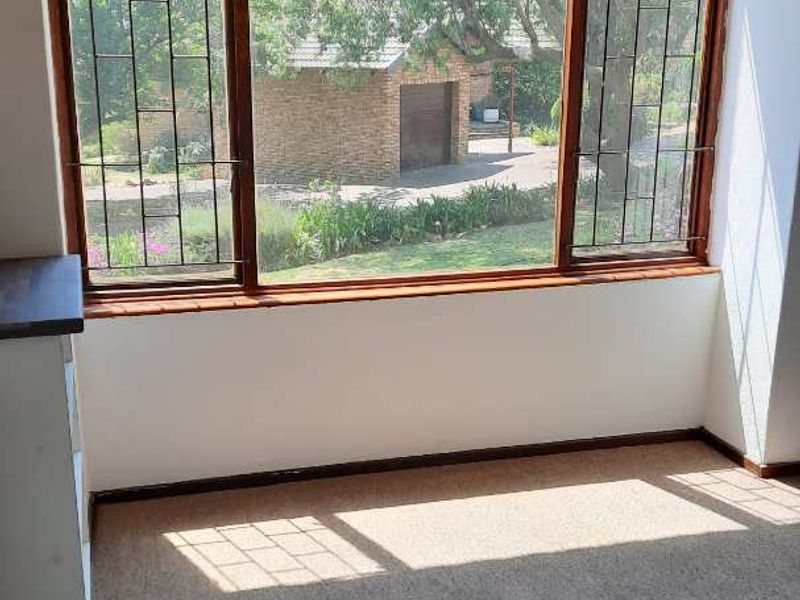 A bright, empty living area featuring a large bay window with security bars, overlooking the garden and driveway.
