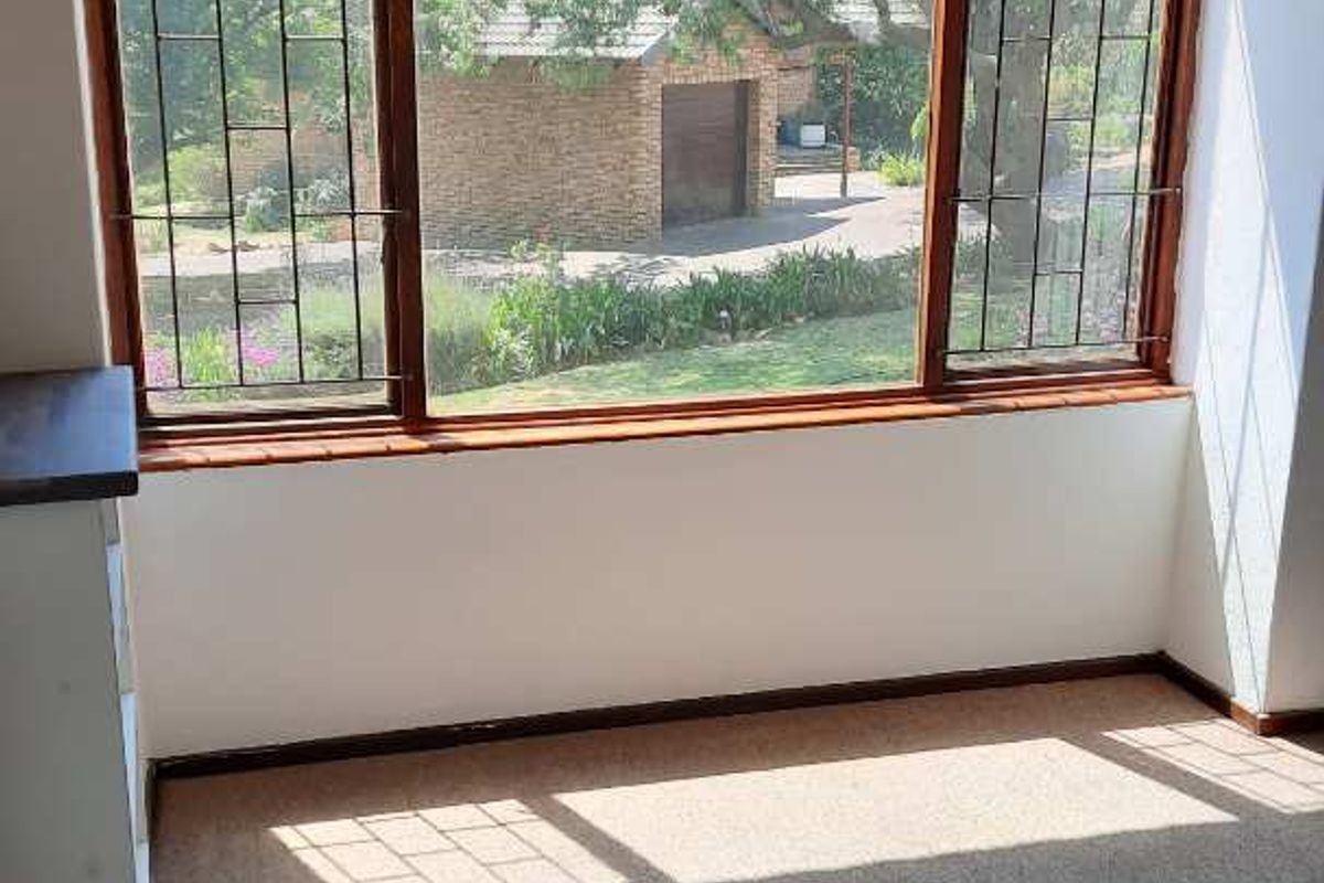 A bright, empty living area featuring a large bay window with security bars, overlooking the garden and driveway.