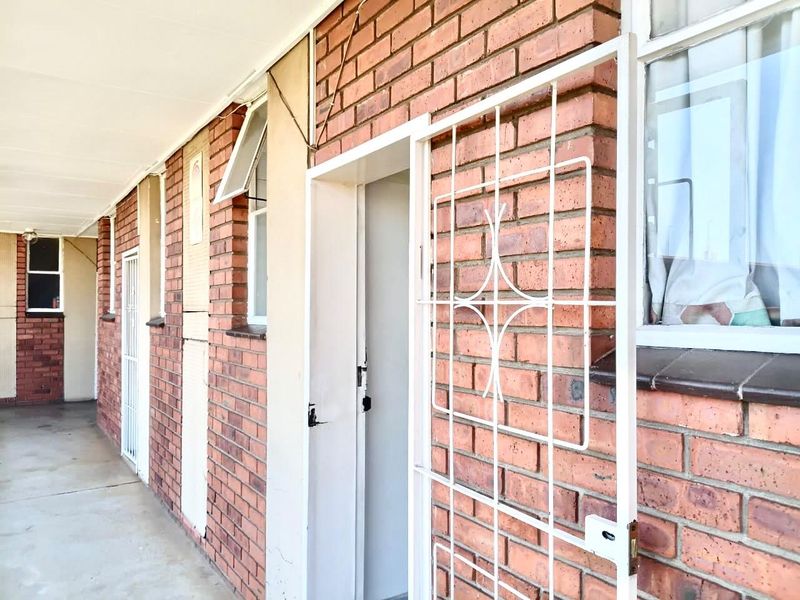 Exterior view of an apartment building entrance featuring a brick facade, security gate, and concrete walkway.