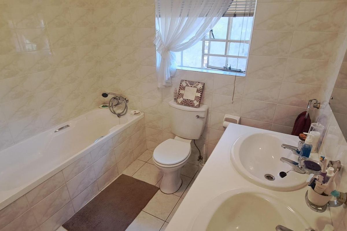 A functional bathroom featuring a built-in bathtub, dual vanity basins, and tiled finishes throughout, offering a practical layout for daily use.