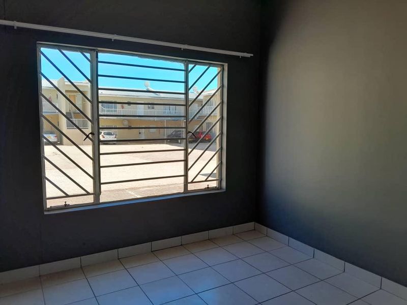 An empty bedroom featuring tiled flooring, dark grey walls, and a window fitted with security bars.