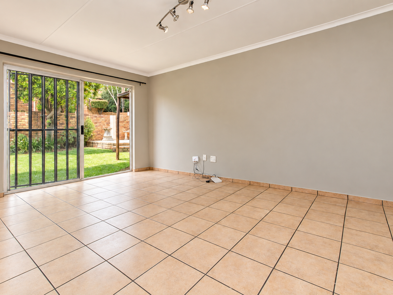 A bright, empty living room featuring neutral tiled flooring, track lighting, and a sliding glass door providing direct access to the rear garden.