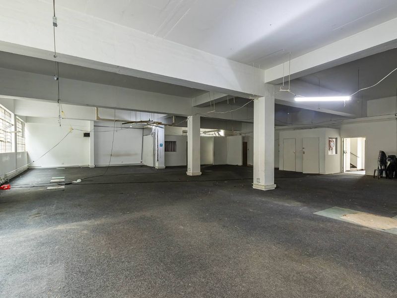 A large, open-plan industrial space featuring exposed concrete beams, industrial-style windows, and carpeted flooring, suitable for a variety of commercial or creative uses.