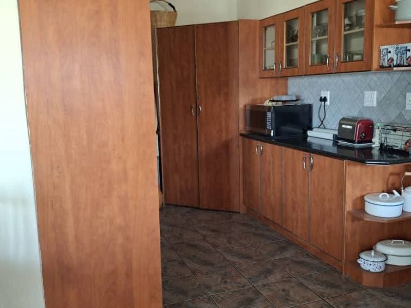 A functional kitchen featuring wood-look laminate cabinetry, dark granite countertops, a tiled backsplash, and durable ceramic floor tiles.