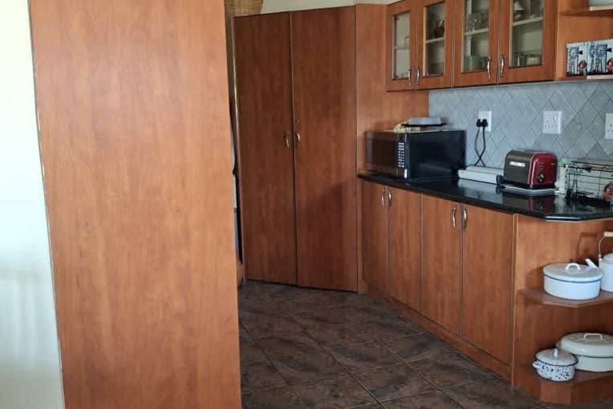 A functional kitchen featuring wood-look laminate cabinetry, dark granite countertops, a tiled backsplash, and durable ceramic floor tiles.